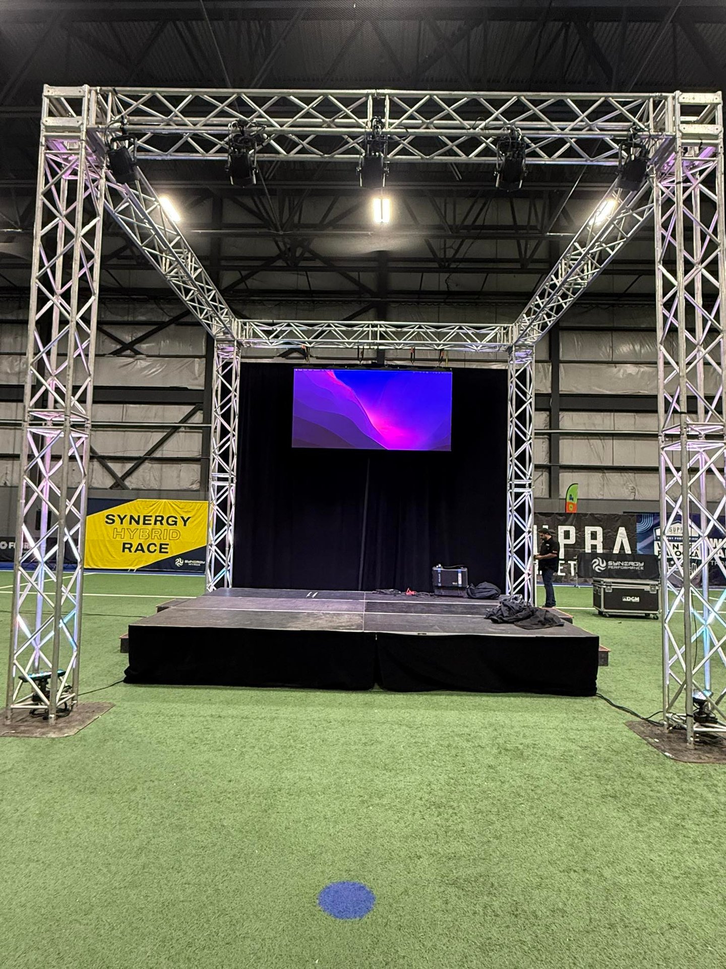Professional event stage with aluminum lighting truss, black backdrop, and LED screen for a hybrid race.
