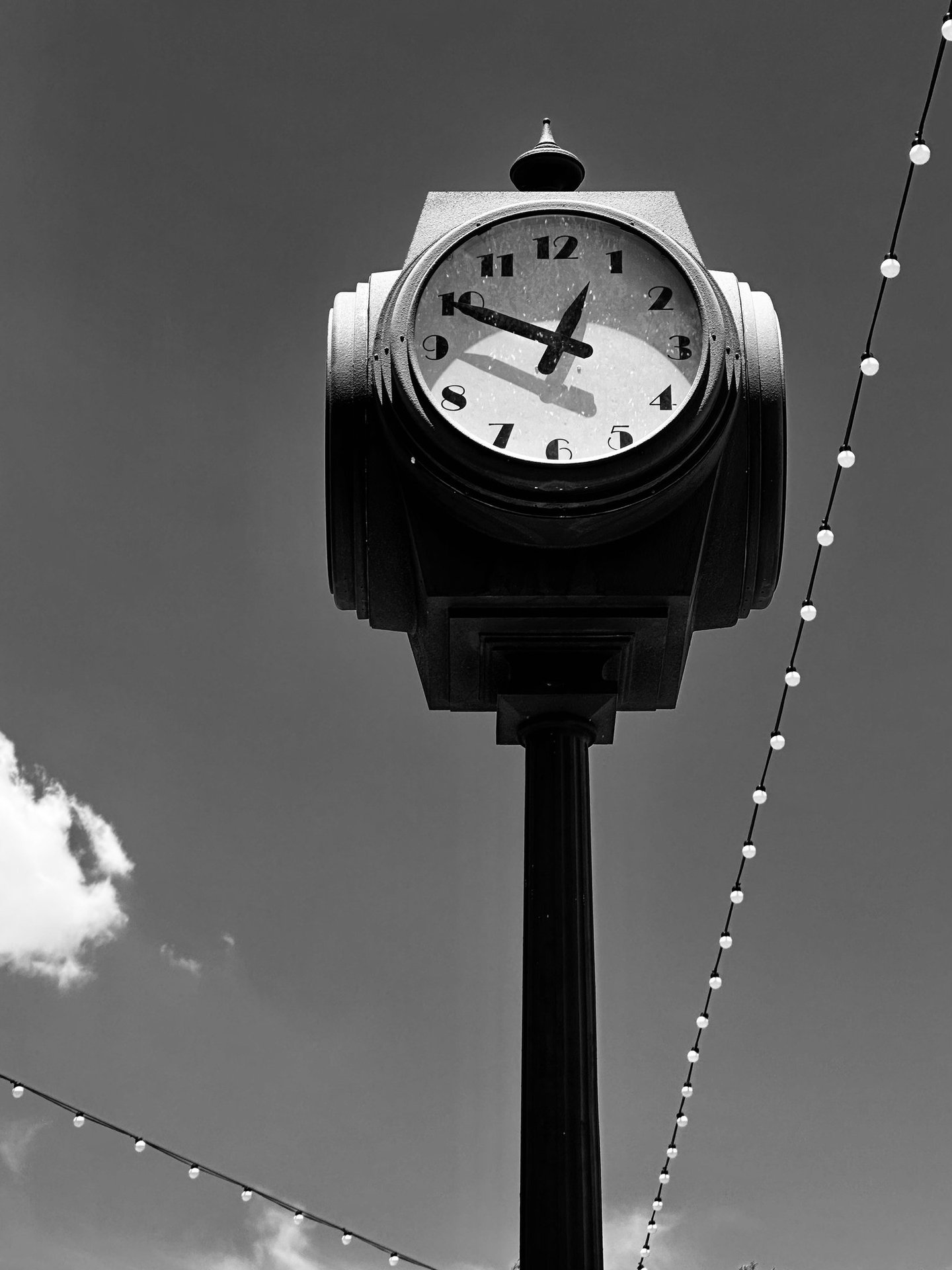 A black-and-white photograph of a vintage street clock mounted on a tall post against a clear sky.