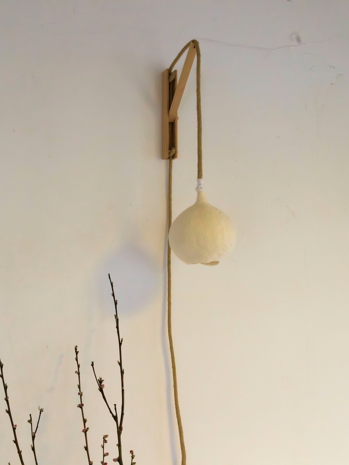 Handgemaakte vilten wandlamp Luminosa in maat S, bevestigd aan een houten houder.