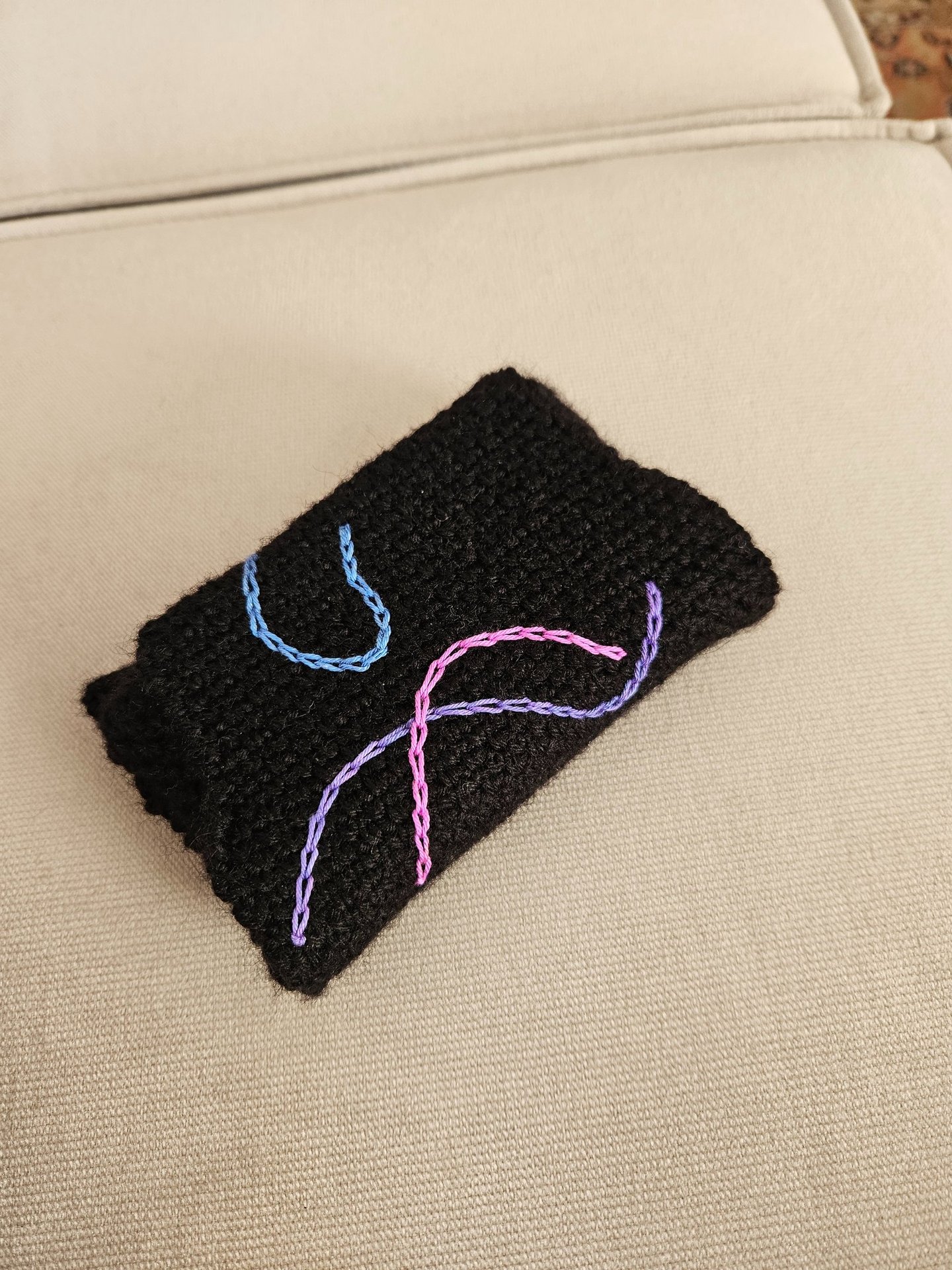 Handmade black crochet pouch with blue and purple embroidered abstract swirl patterns.