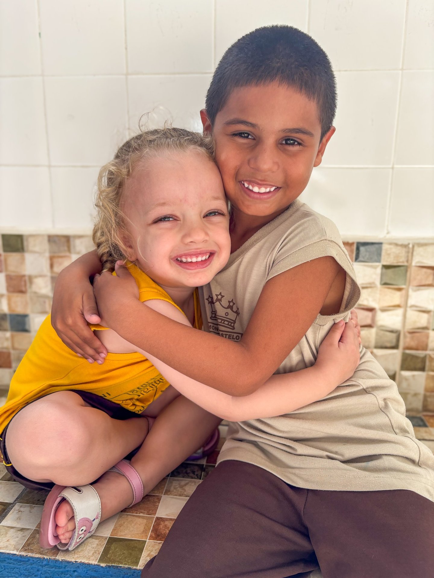 a boy and girl hugging each other on a tiled floor