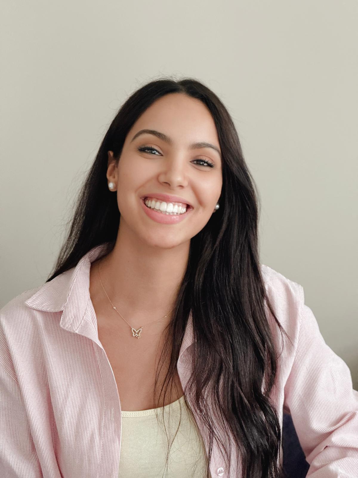 A smiling young woman with long dark hair wearing a pink striped shirt and a butterfly necklace.