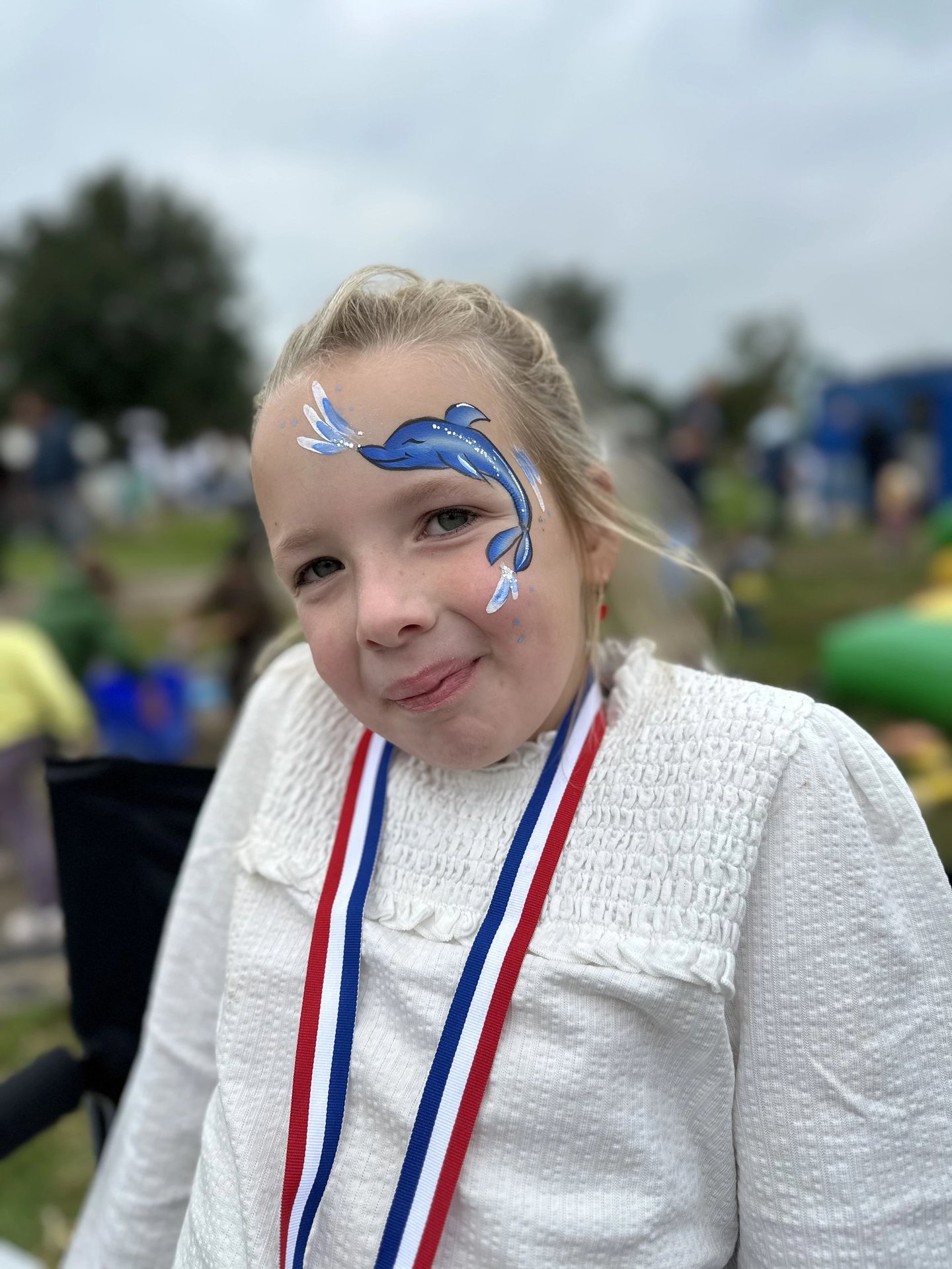 Meisje met een gedetailleerde blauwe dolfijn op haar gezicht geschminkt.