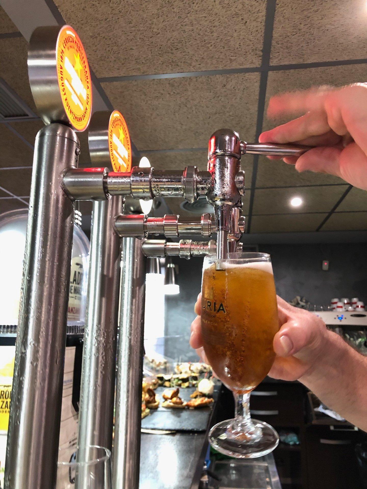A bartender pouring a cold draft beer from a chrome tap into a glass at a Spanish tapas bar.