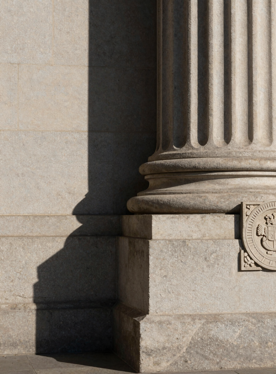 Close-up architectural shot of a courthouse exterior column base, deep shadow and worn stone texture under flat midday light, official carved seal partially visible at the right edge, generous negative space of stone wall to the left