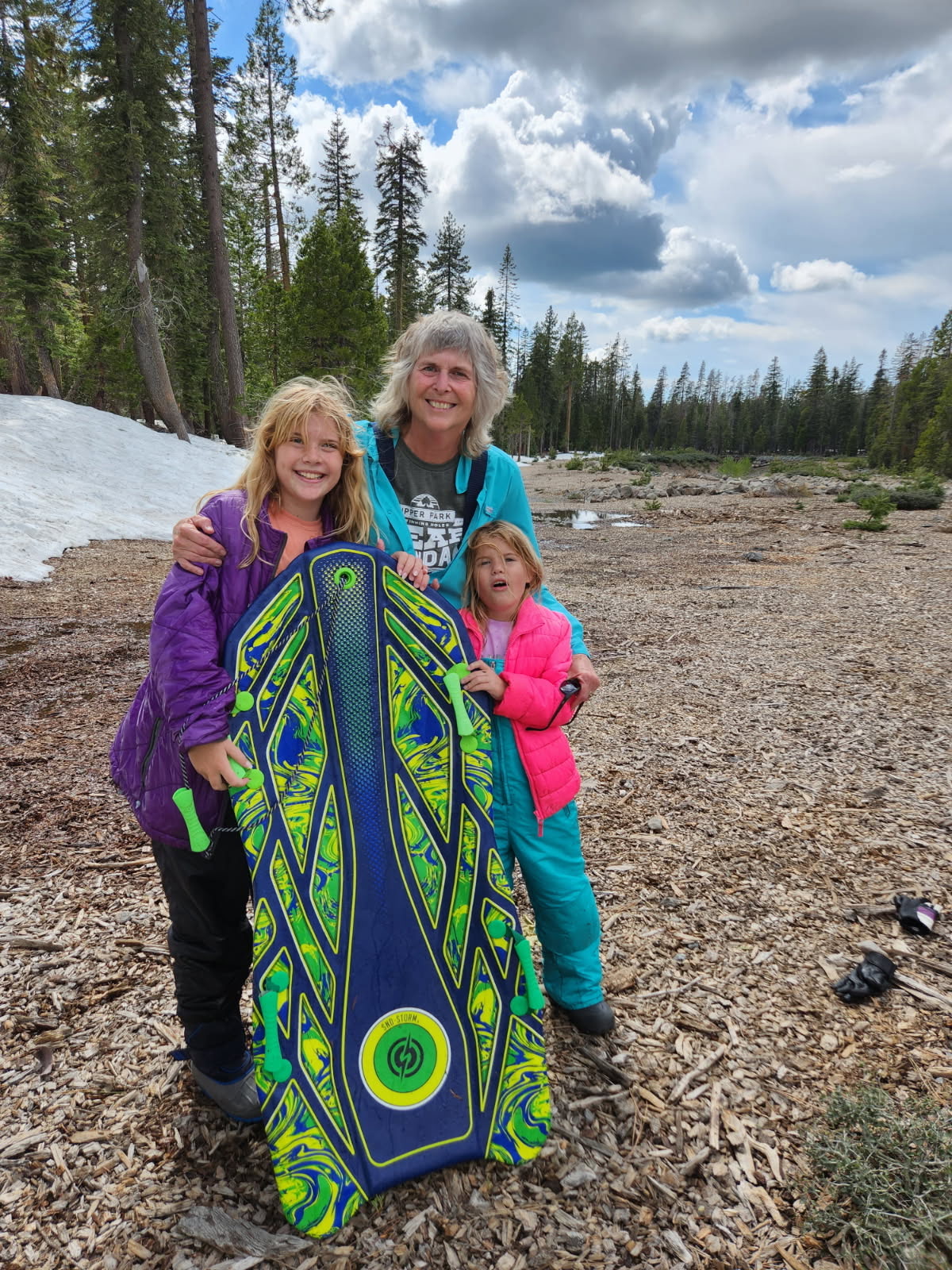 Teresa, Cecelia, and Mary Grace holding a sled by the snow and lake