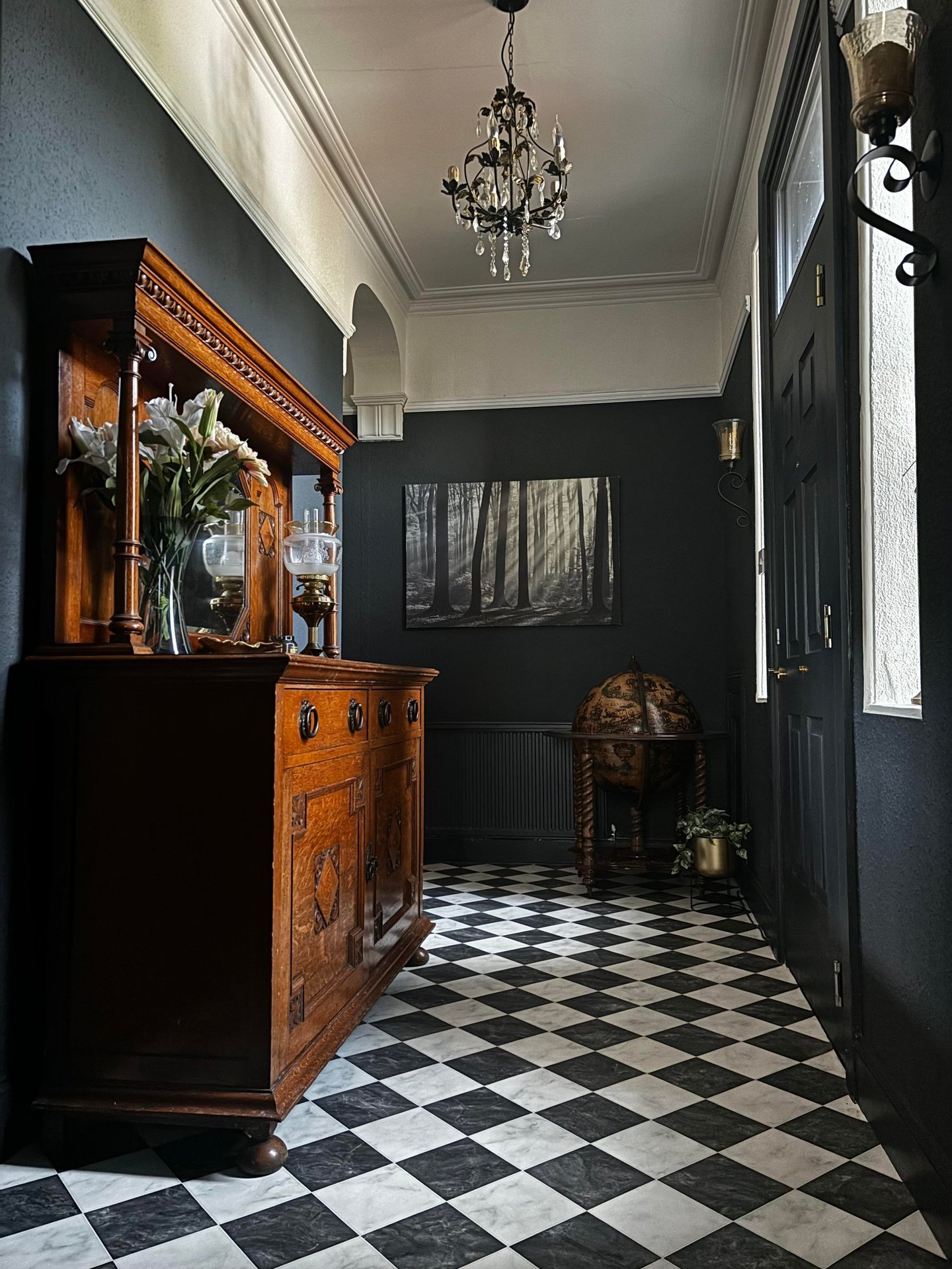 Elegant dark hallway with checkered floor, antique wooden sideboard, and crystal chandelier.