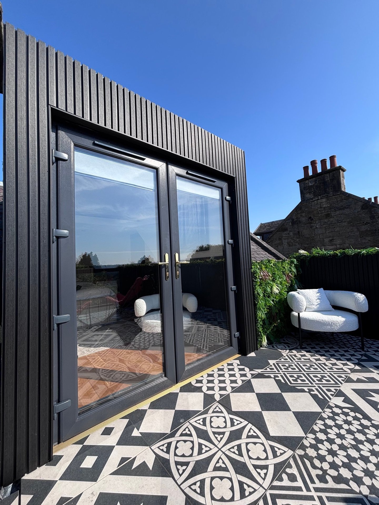 Modern rooftop balcony with black slat cladding and glass french doors on a patterned tile patio.