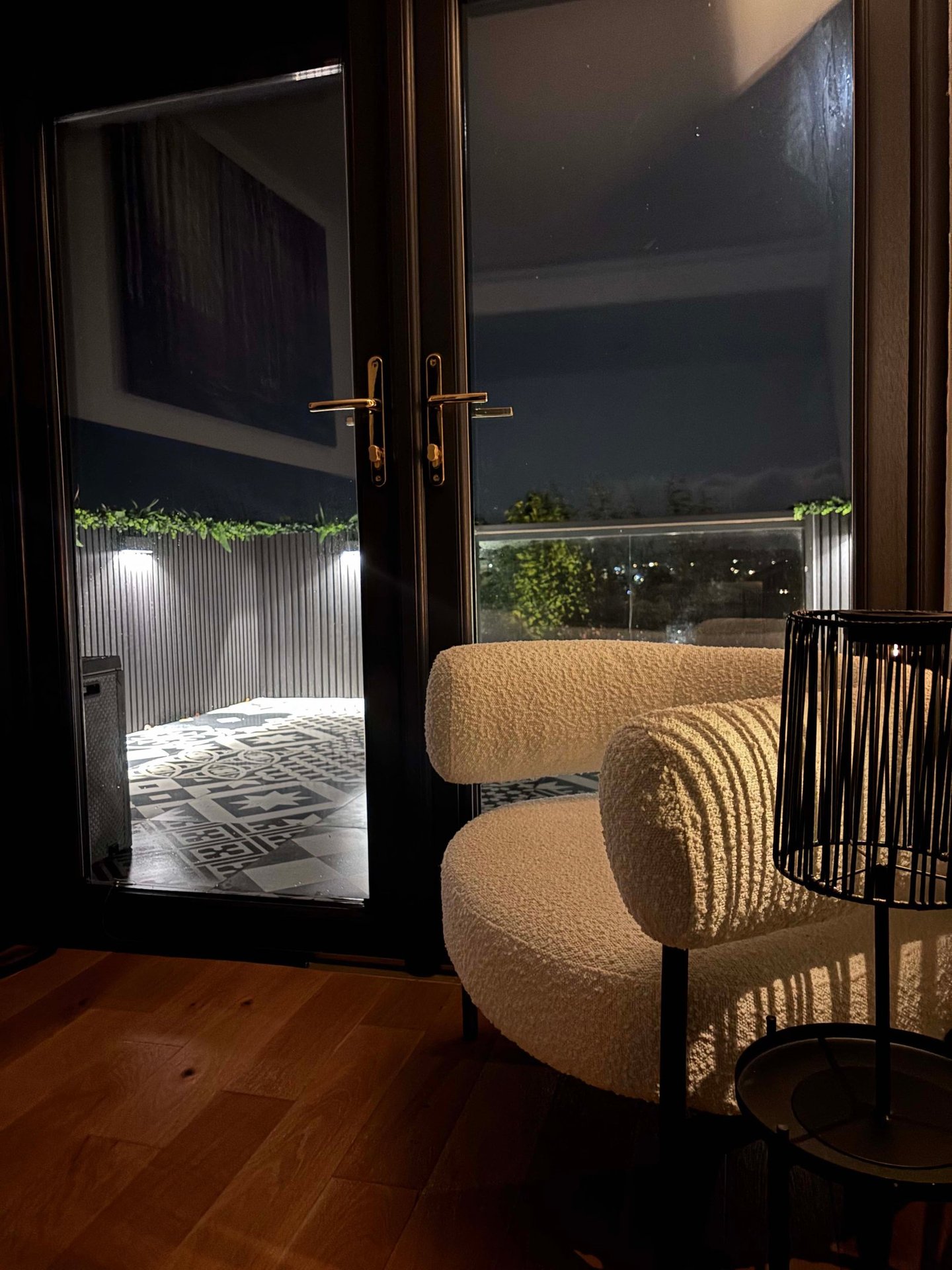 Modern white boucle armchair by glass balcony doors overlooking a lit outdoor patio at night.