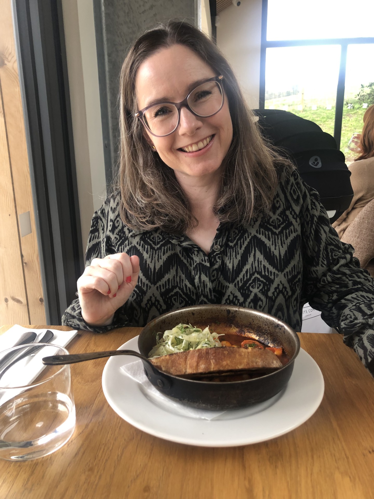 a woman with glasses smiles. She is out for lunch.