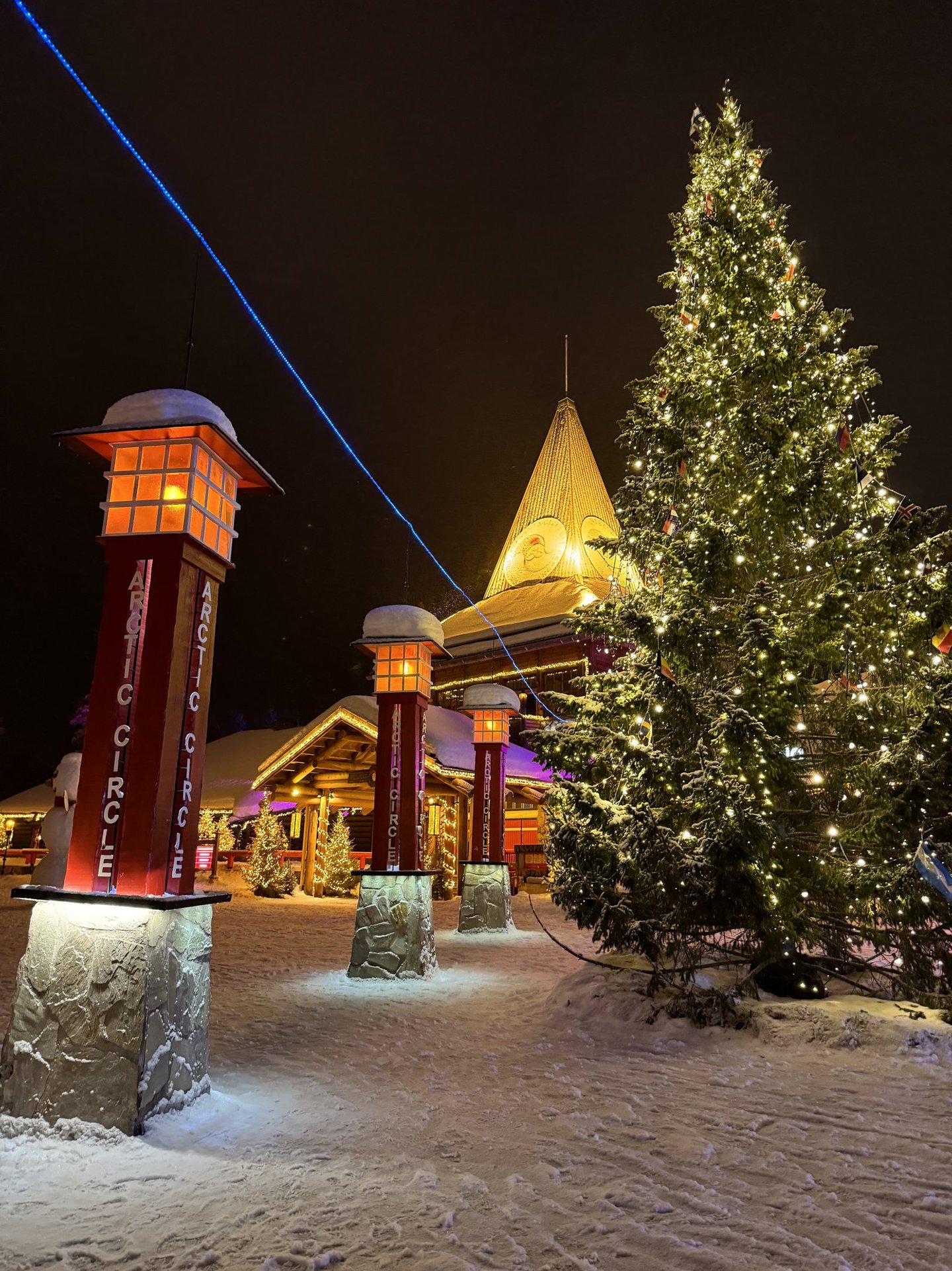 Illuminated Christmas tree and Arctic Circle pillars at Santa Claus Village in Lapland, Finland at night.