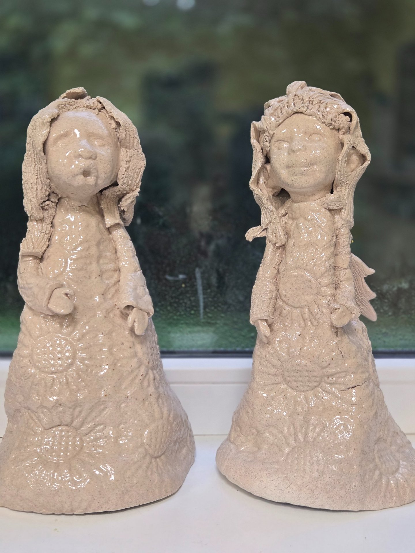 Two handmade ceramic angel figurines with glazed finishes on a windowsill.