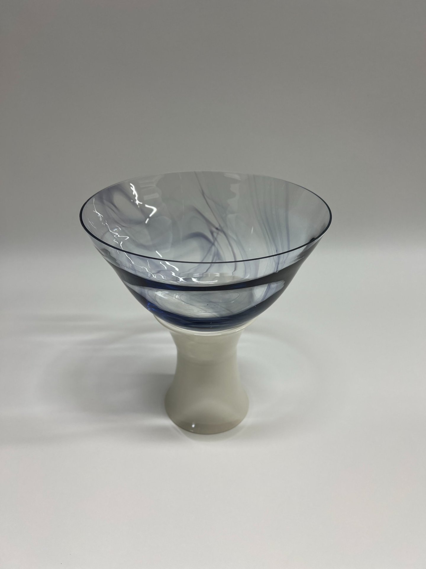 Large and wide blown glass bowl, with swirls of ink blue glass, on a white porcelain ceramic base. 