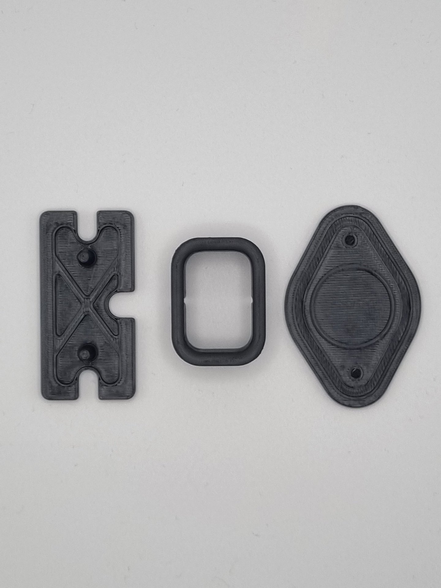 Three black 3D printed mechanical components including a bracket, spacer, and mounting plate.