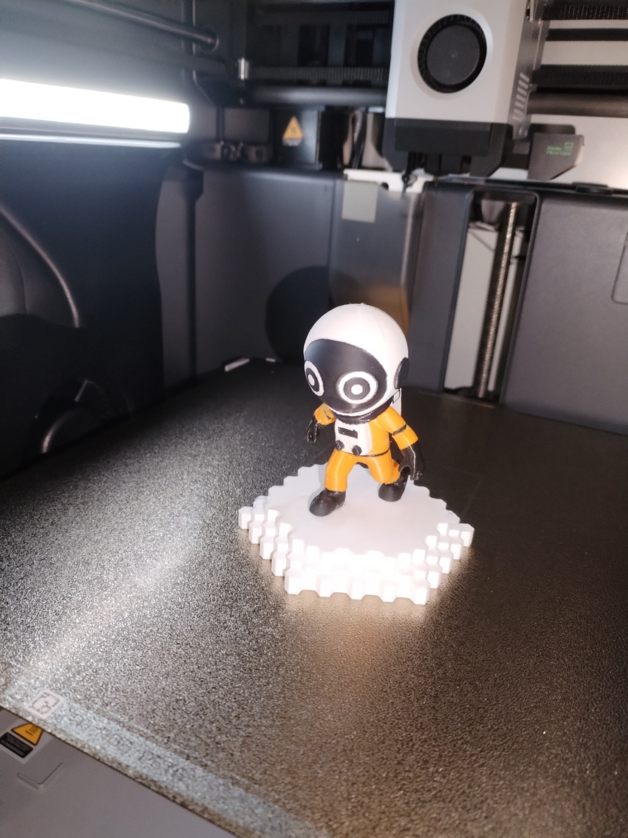 Figurine d’astronaute imprimée en 3D par OptiPrint3D, en combinaison orange sur socle blanc.