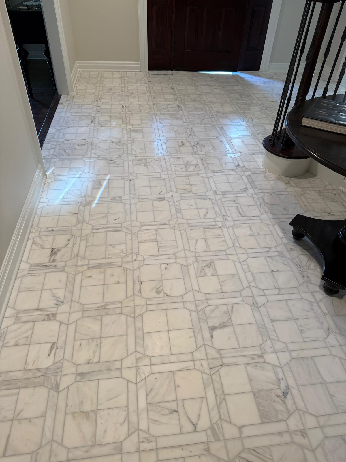 Elegant foyer entryway featuring a luxury white marble tile floor with an intricate geometric inlay pattern.