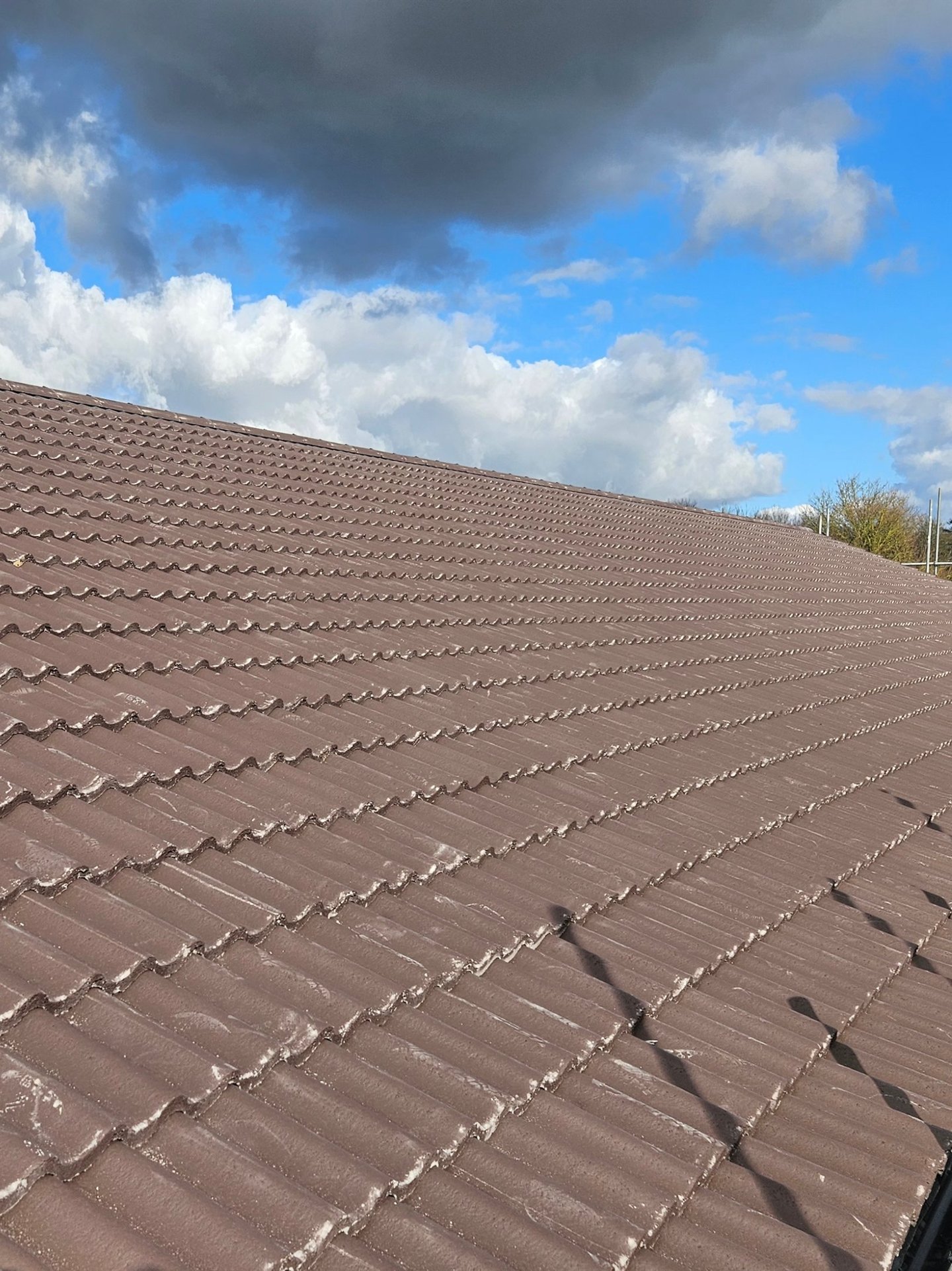 A clean, newly installed brown concrete tile roof under a blue sky with white clouds.