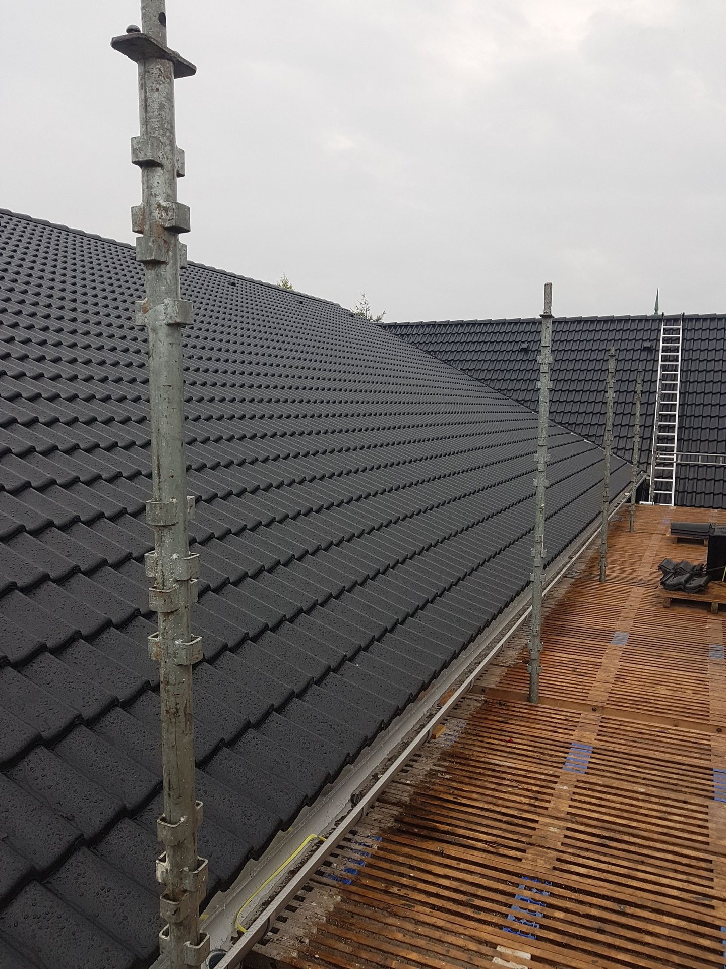 Professionel montering af sorte tagsten på et beboelseshus med sikkerhedsstillads.