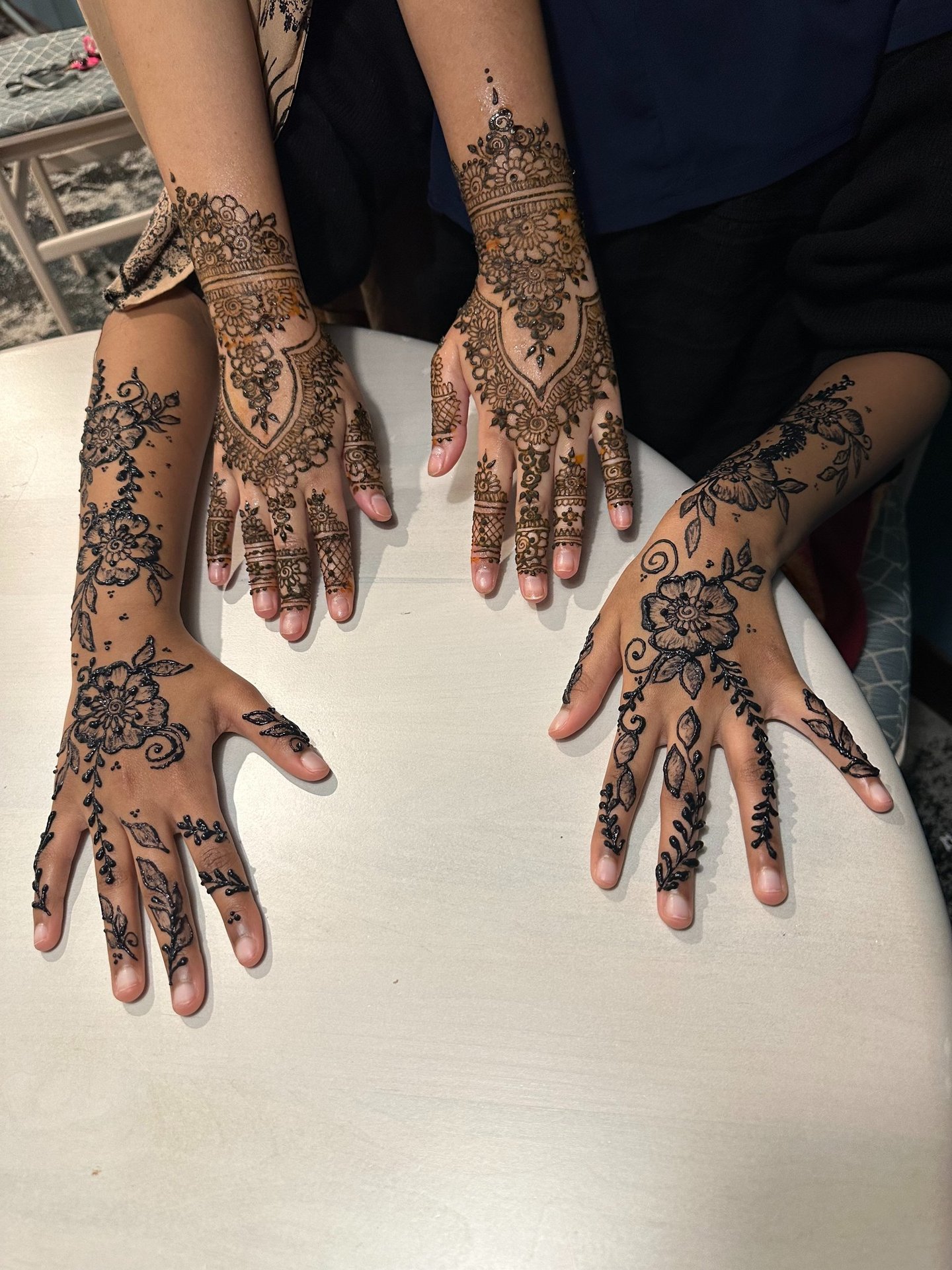 two hands rest next to each other on a table with intricate designs on them, one henna and one jagua