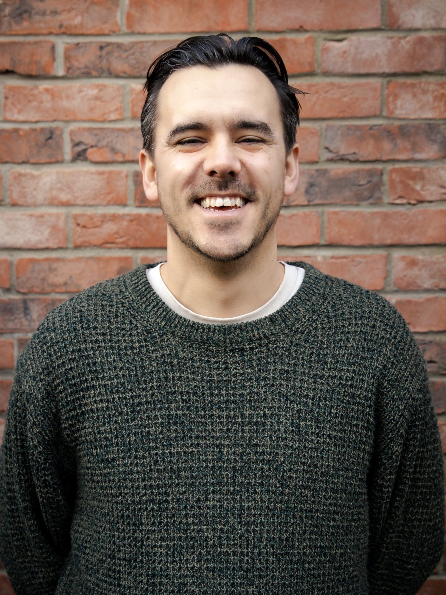 a man smiling in front of a brick wall background