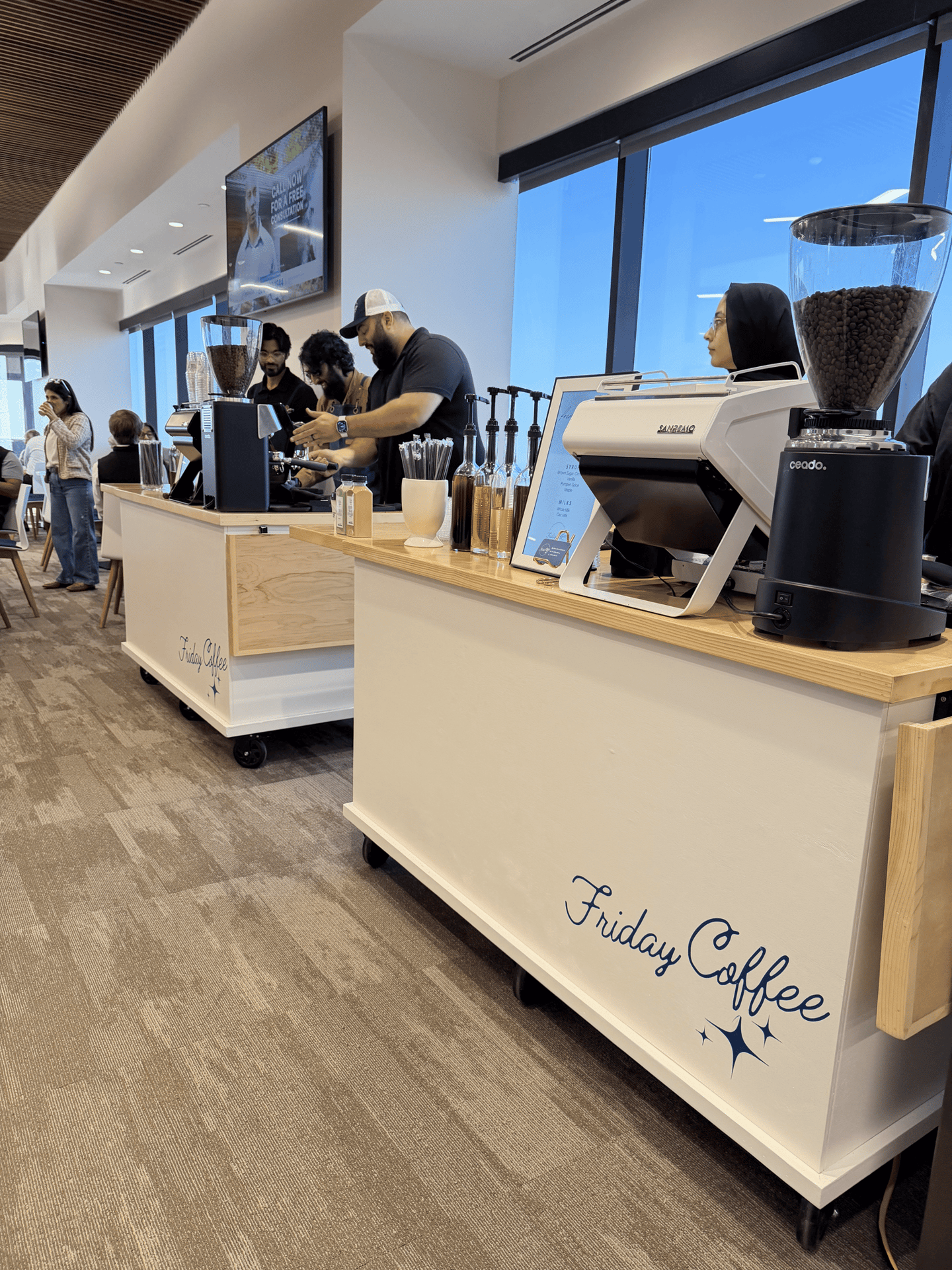 Professional baristas preparing espresso drinks at a Friday Coffee mobile catering cart in a modern office lobby.