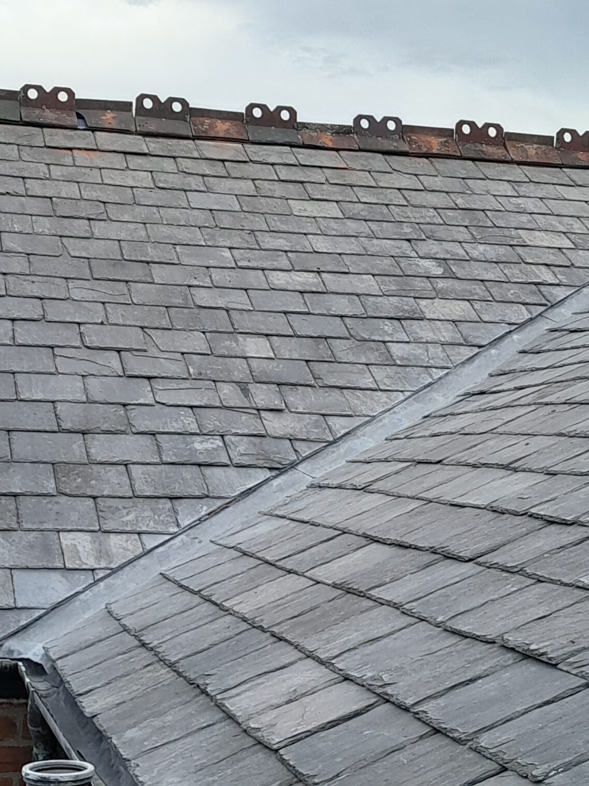 A weathered grey slate roof featuring a lead valley gutter and decorative ridge tiles.