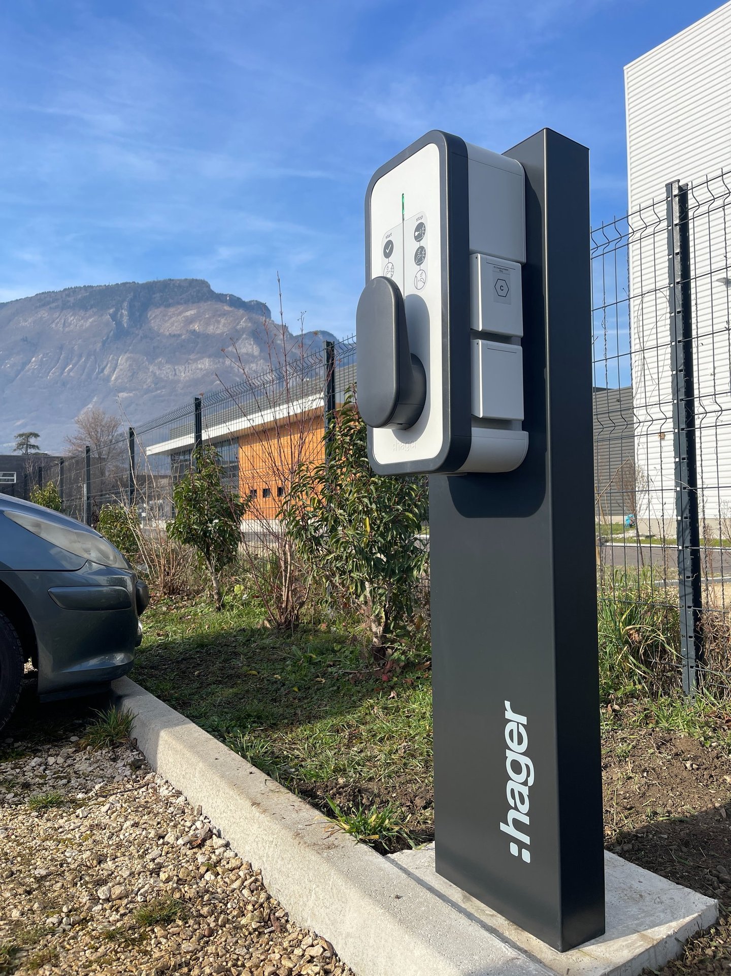 a parking meter with a car parked in front of a fence