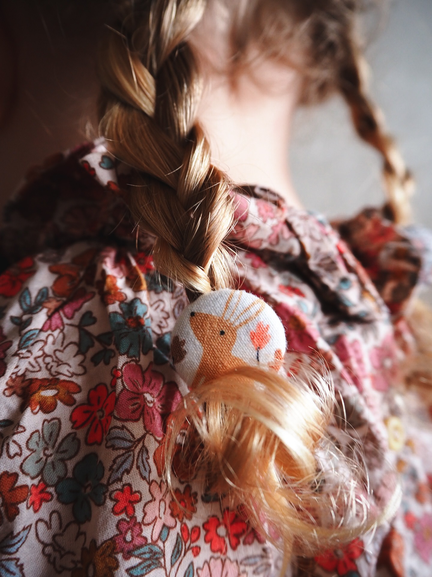 gumka do włosów z królikiem zaplątana na warkoczu na tle bluzki w kwiaty
