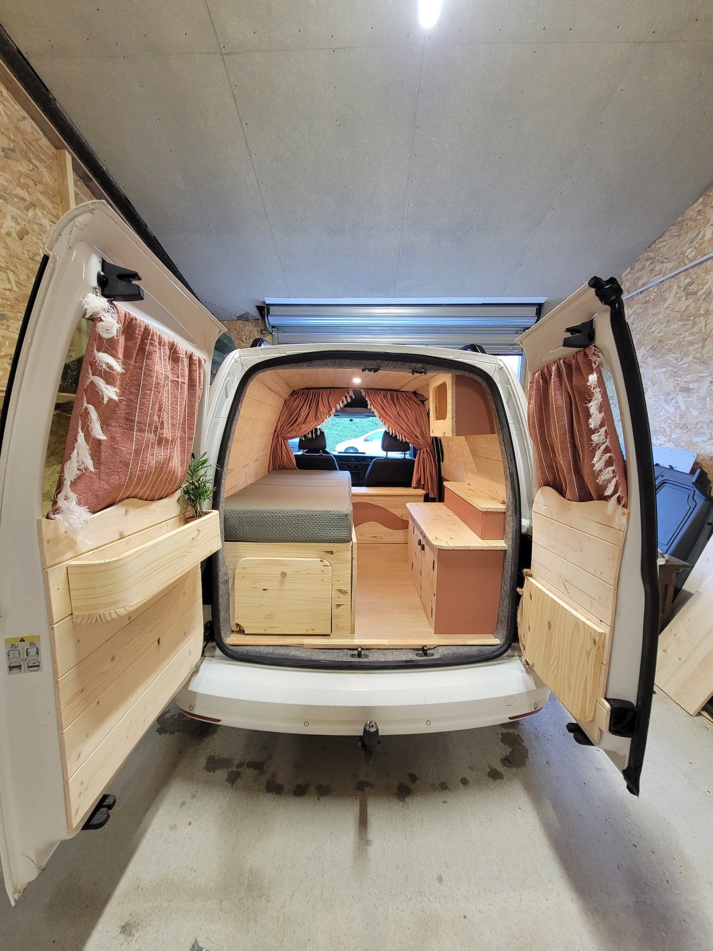 Aménagement complet d'un fourgon blanc en bois clair avec rideaux terracotta et lit peigne, réalisé