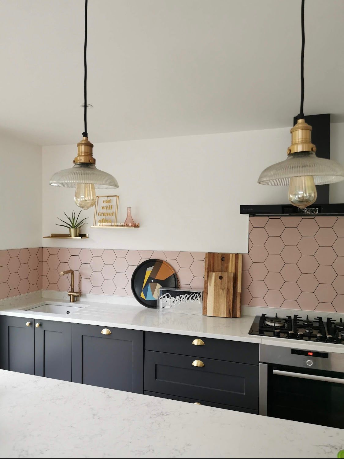 Modern kitchen featuring black cabinets, pink hexagon tile backsplash, and industrial glass pendant lights.