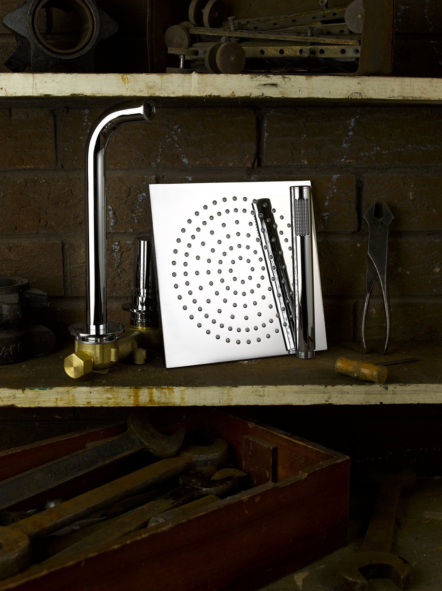 square chrome rain shower head and tap on a shelf in an old workshop