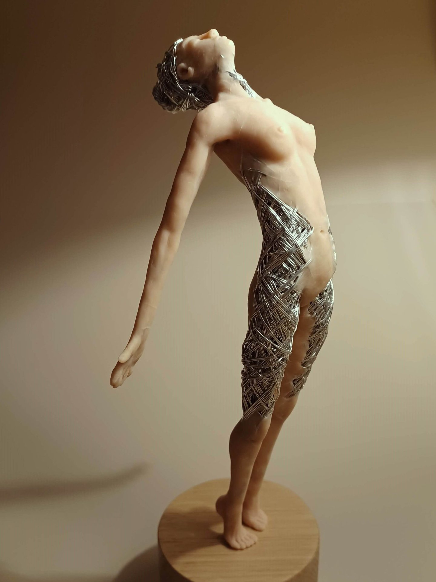 A detailed polymer clay and wire sculpture of a standing female figure, stretching with arms back