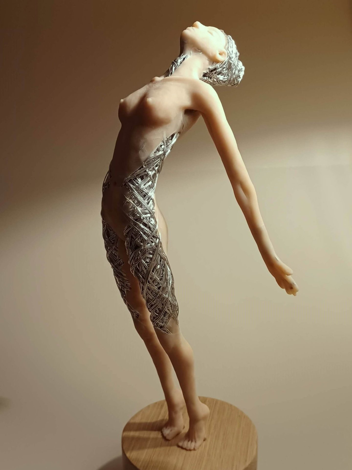 A detailed polymer clay and wire sculpture of a standing female figure, stretching with arms back