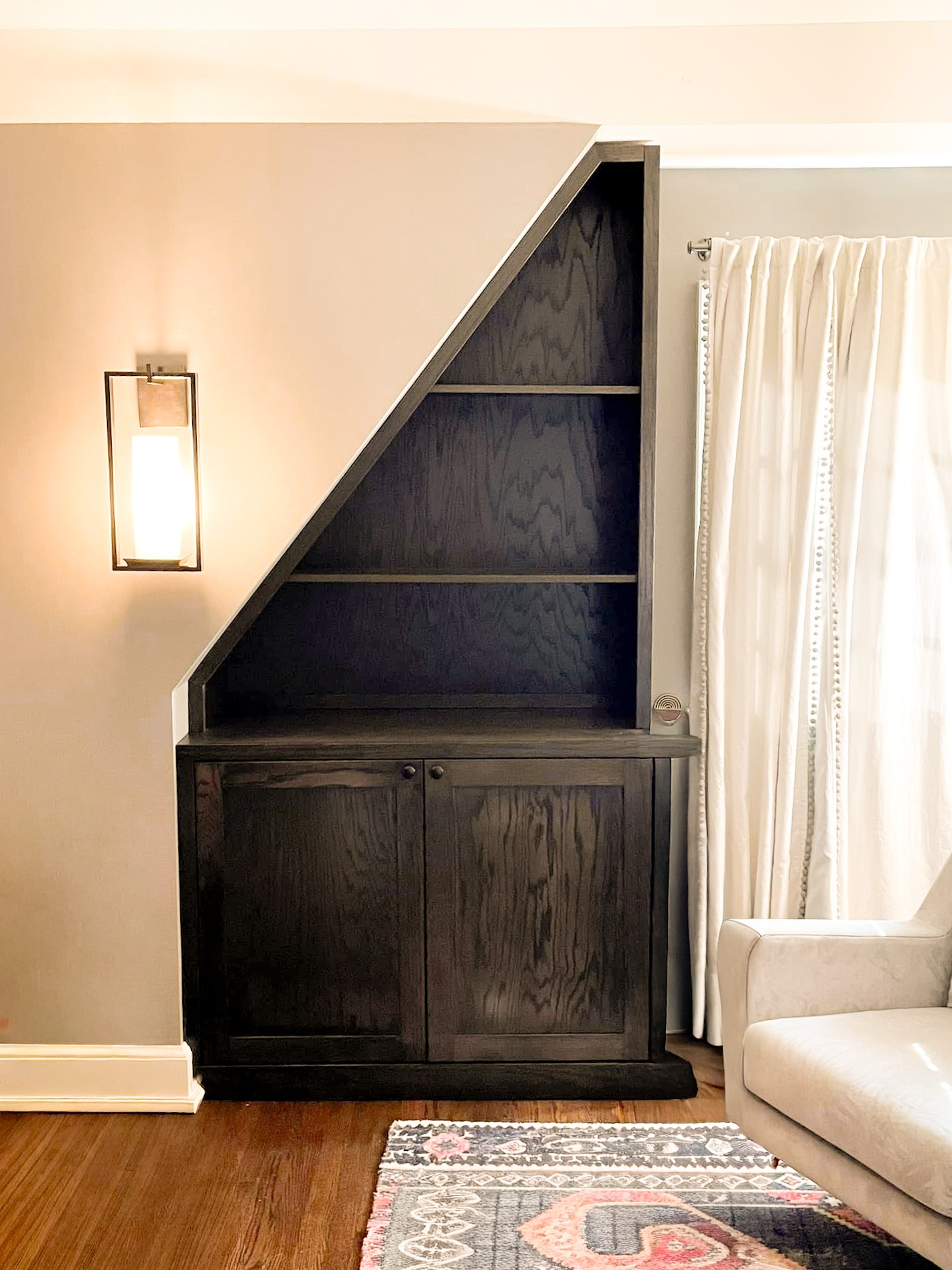 Asymmetrical wooden bookcase and cabinet built in to fit an odd-sized space in a client home.