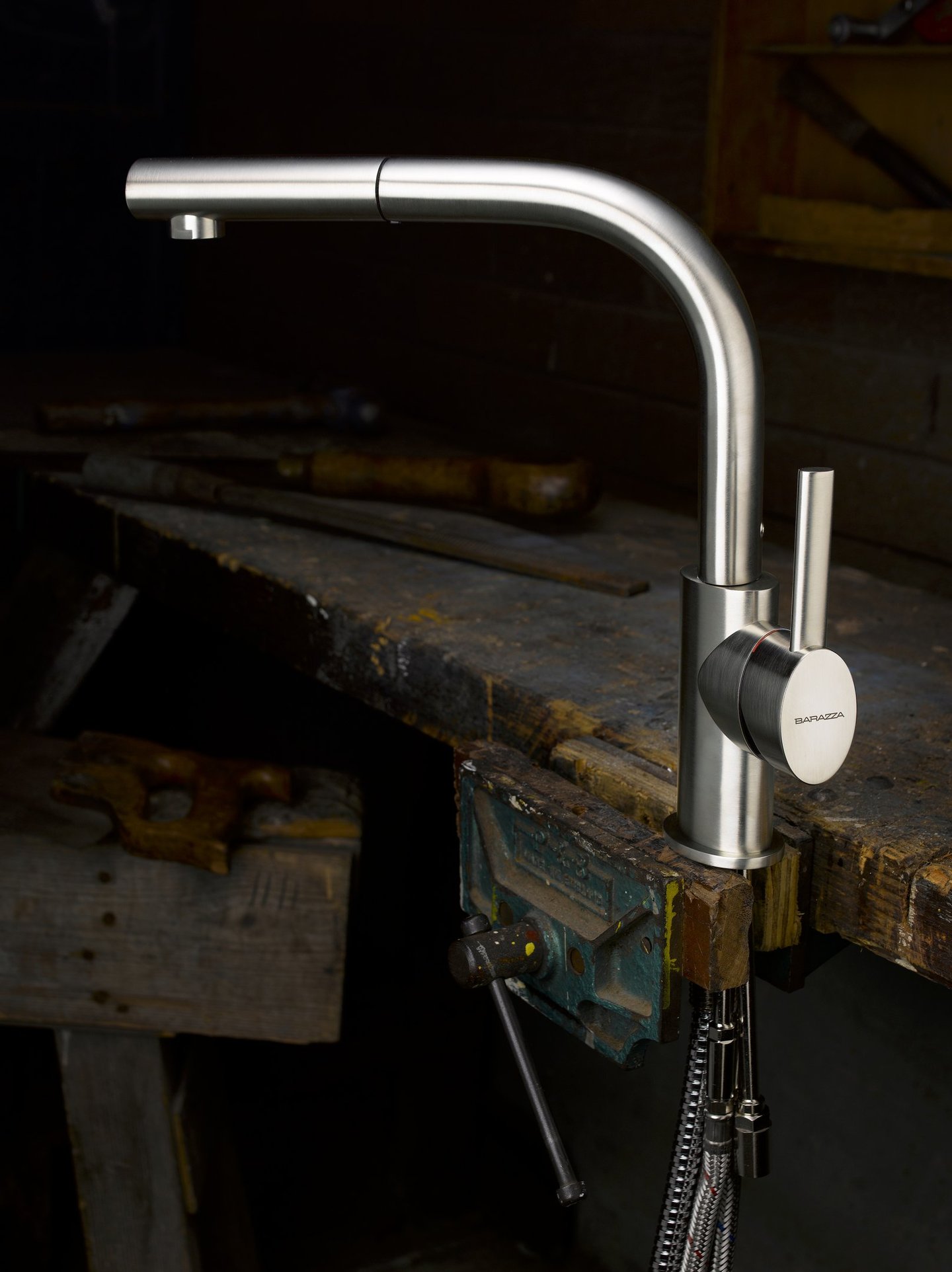 brushed stainless steel kitchen mixer tap held in the vice of an old wooden work bench