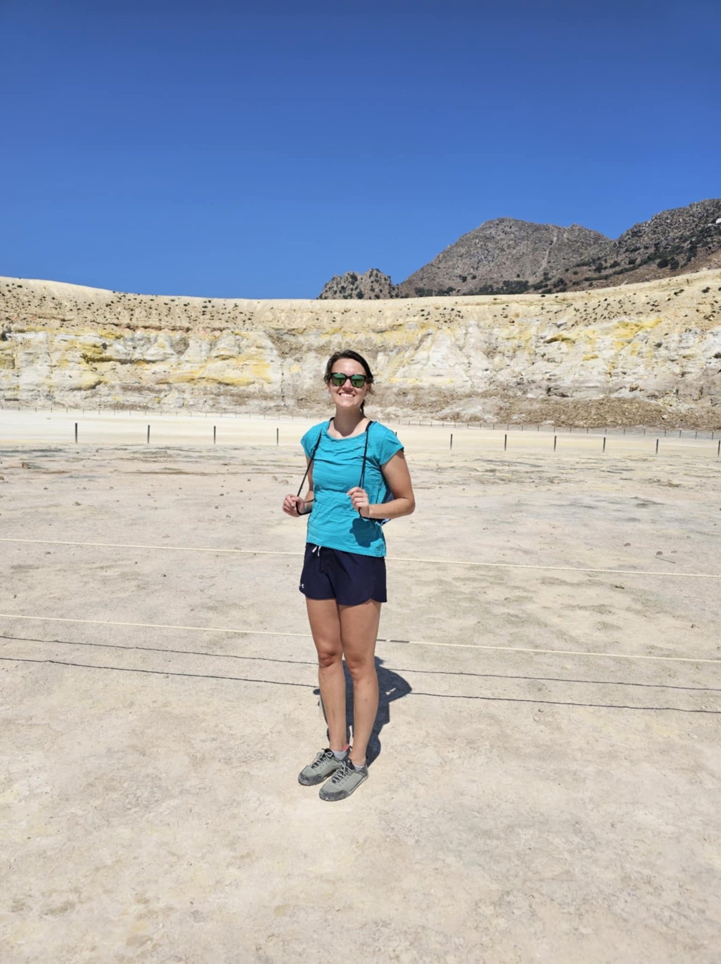 a woman in a blue shirt and sunglasses standing in a desert
