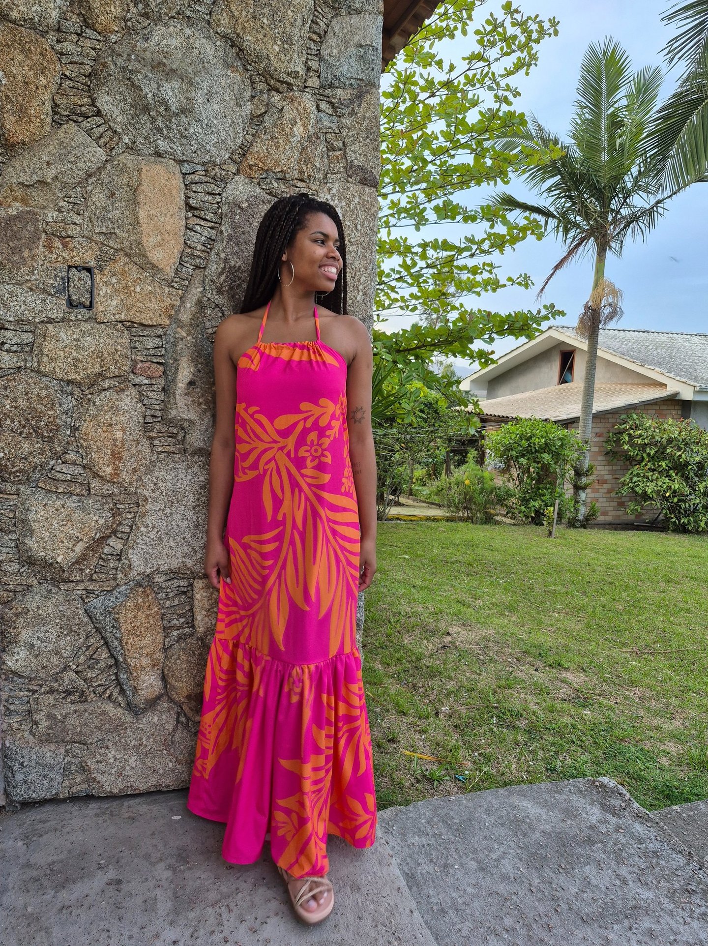 Mulher em pé usando um vestido com babado franzido, estampado nas cores rosa e laranja