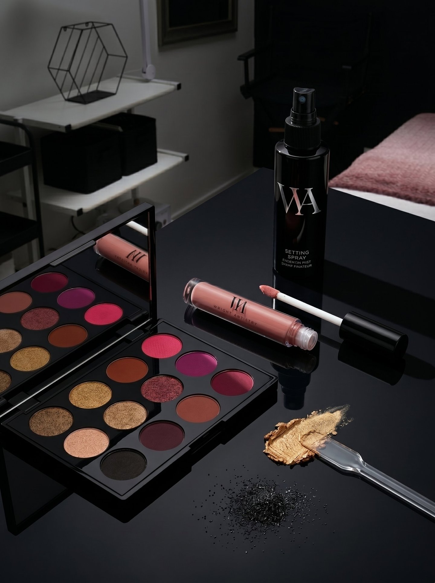 Professional eyeshadow palette with lip gloss and makeup setting spray on a black vanity table.