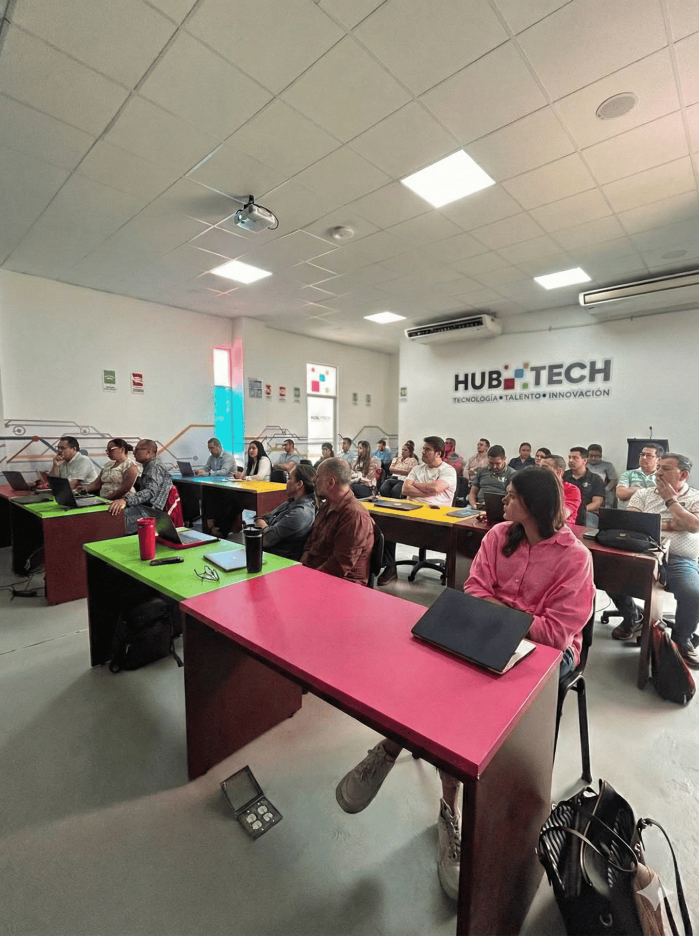 Students attending a technology workshop in a Hub Tech classroom with laptops and colorful desks.