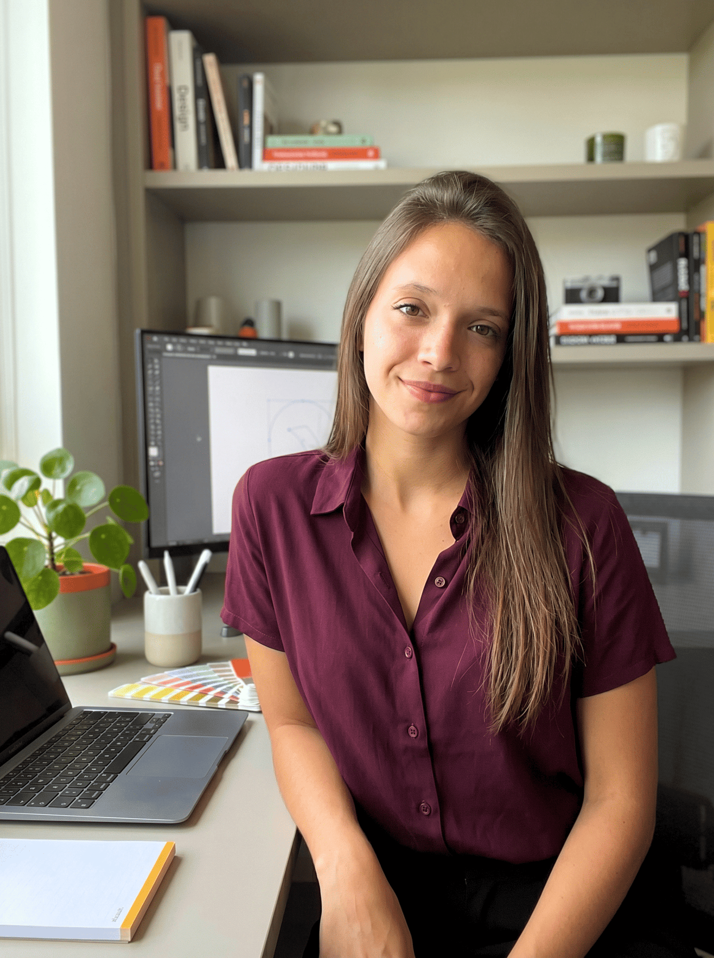 Una diseñadora gráfica sonriente está sentada en su escritorio con una computadora portátil