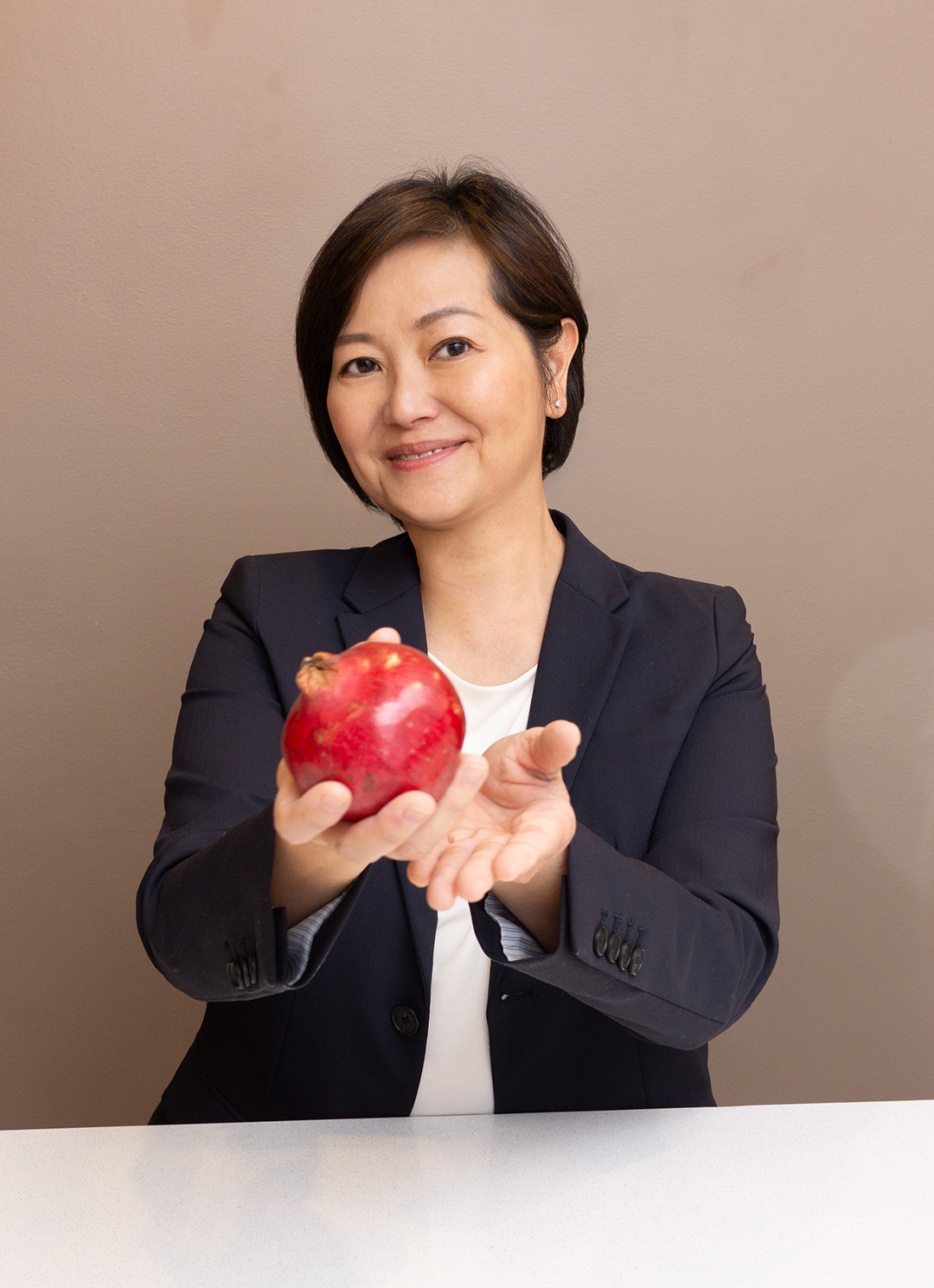 a woman in a dark suit holding a red pomegranate in her hand