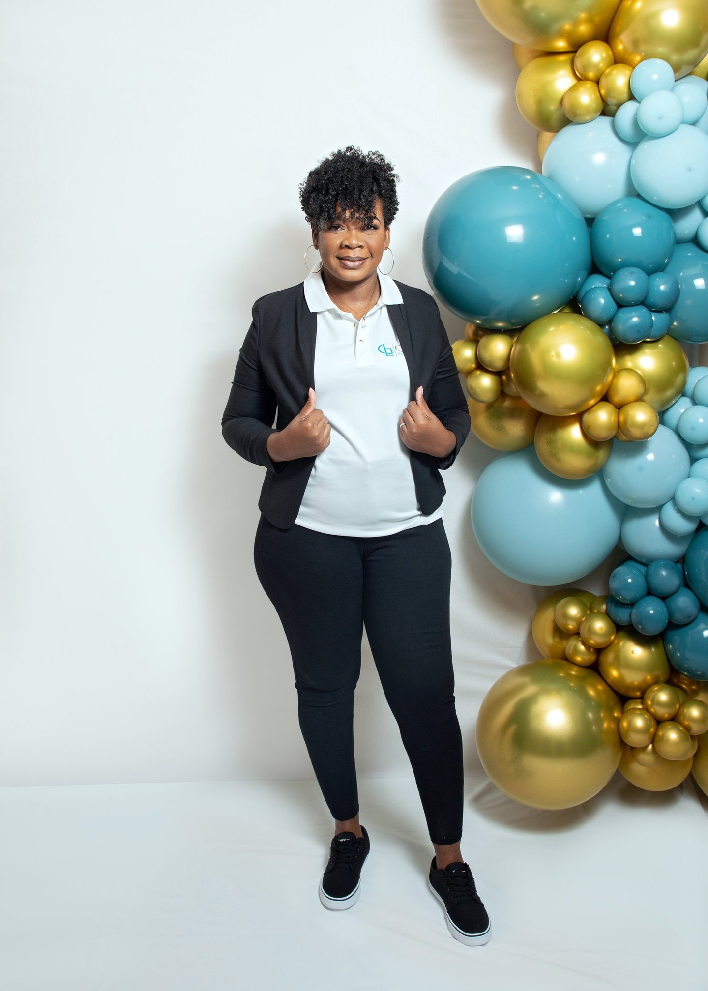 a woman in a black jacket and white shirt stand beside balloon