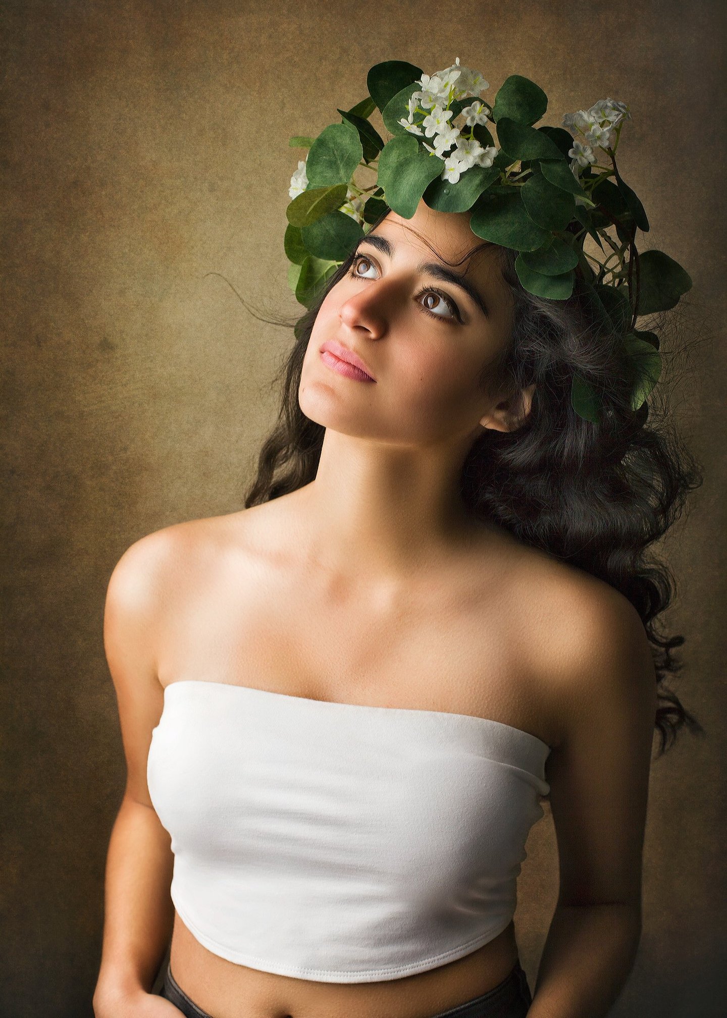 a gorgeous girl with long black curly hair looking up as the wind blows her hair away, she wears a vines crown with flowers