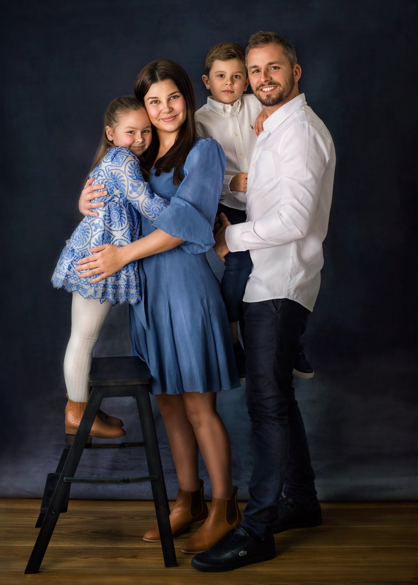 a family of four posing in a studio for a family portrait, all wearing blue and white