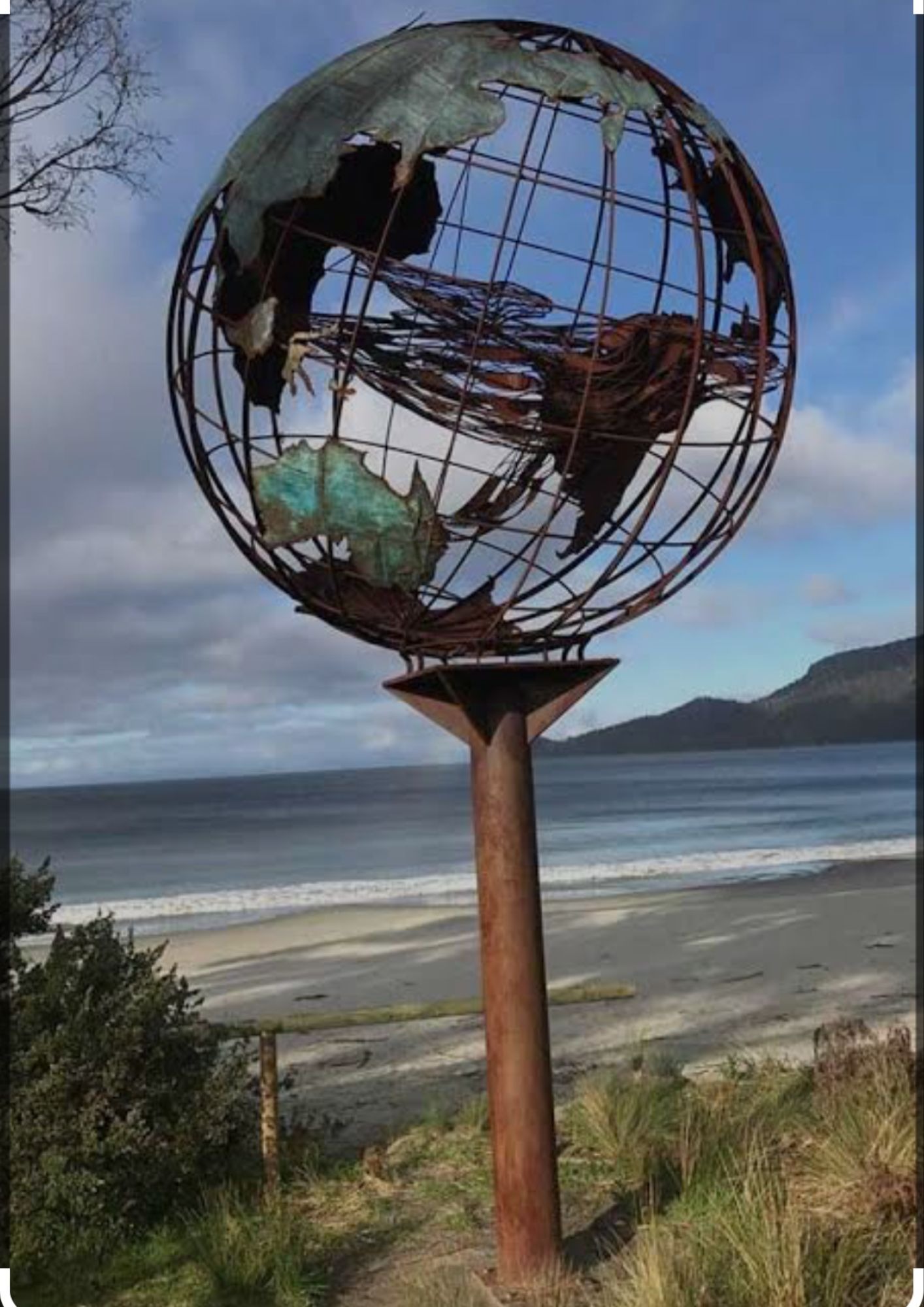 Verdigris metal globe sculpture on the beach with a mother whale and her calf in the middle of it