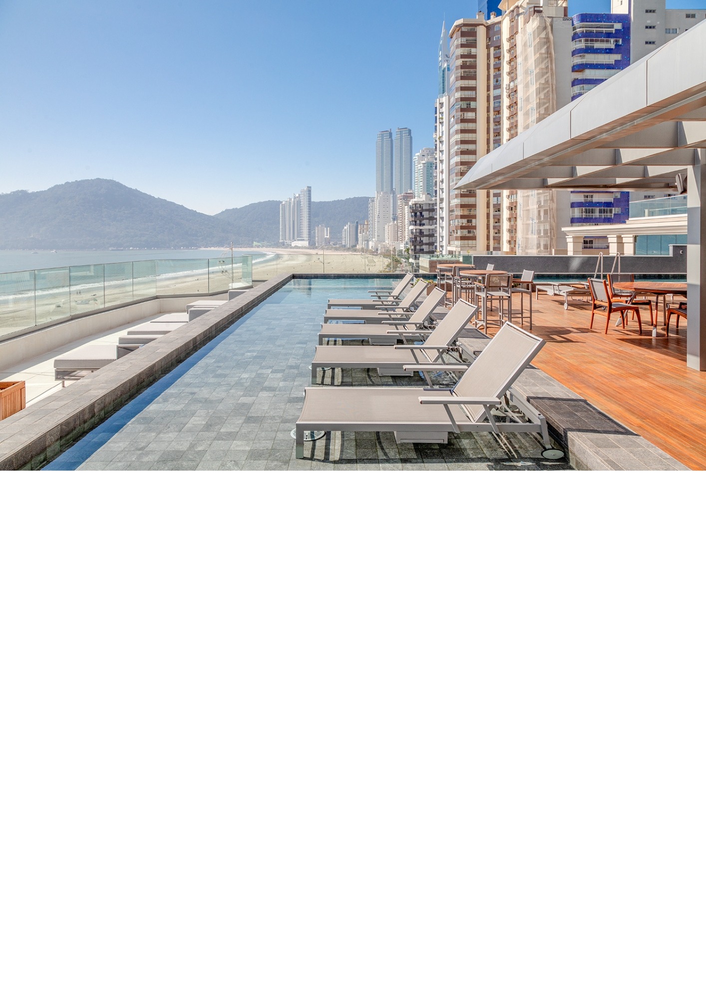 Vista de piscina com cadeiras e a orla de Balneário Camboriú em sua dimensão.