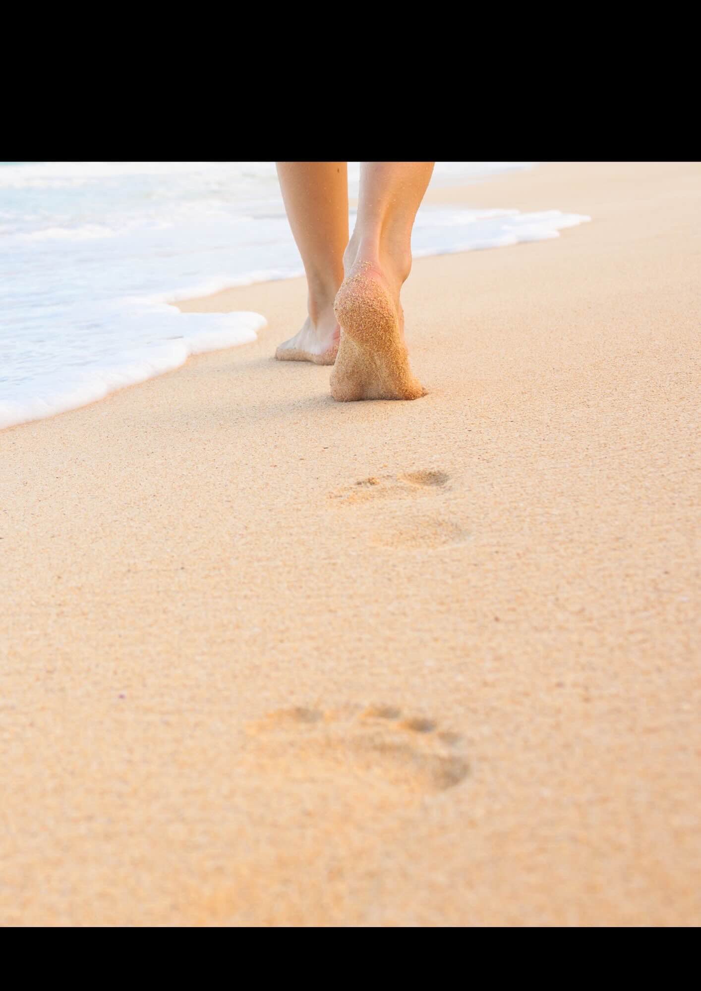 Close-up van voeten op een strand met voetafdrukken in het zand bij de kustlijn.
