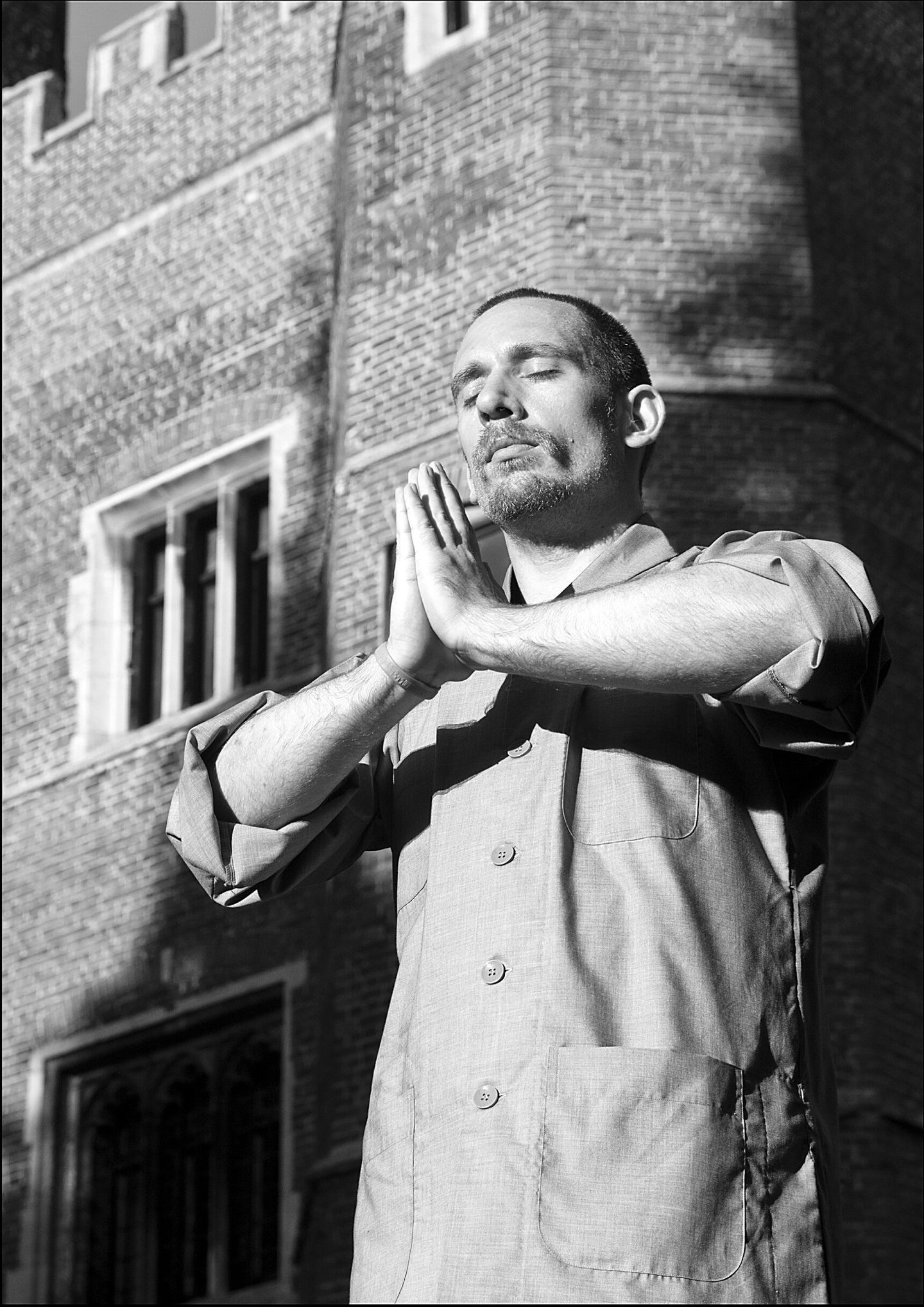 Heng Hu practices mindfulness meditation with hands in prayer position outside a brick building.