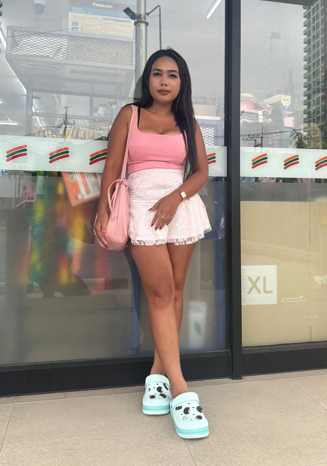 Lady therapist leaning against a shop window wearing short white skirt and sleeveless pink top