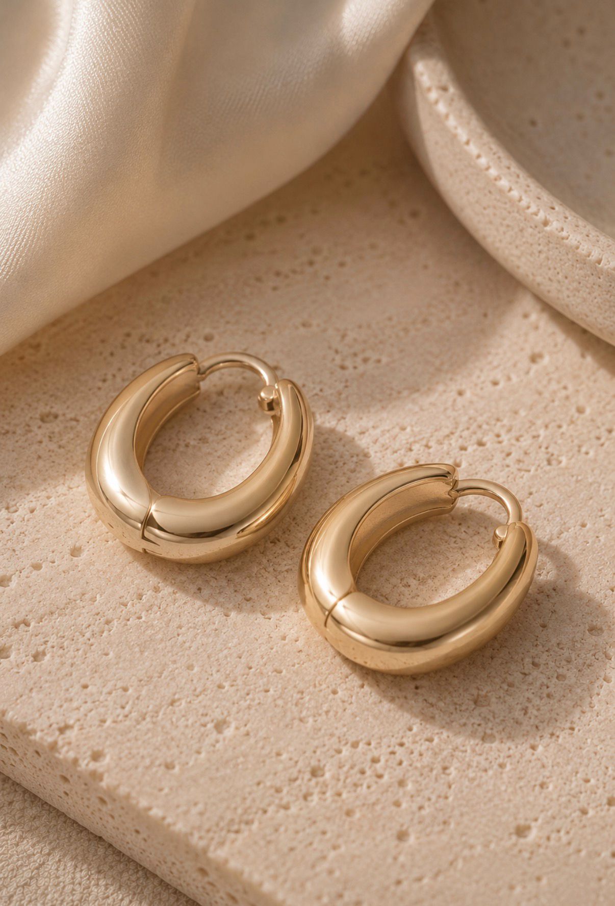 Pair of polished gold hoop earrings displayed on a textured stone surface.